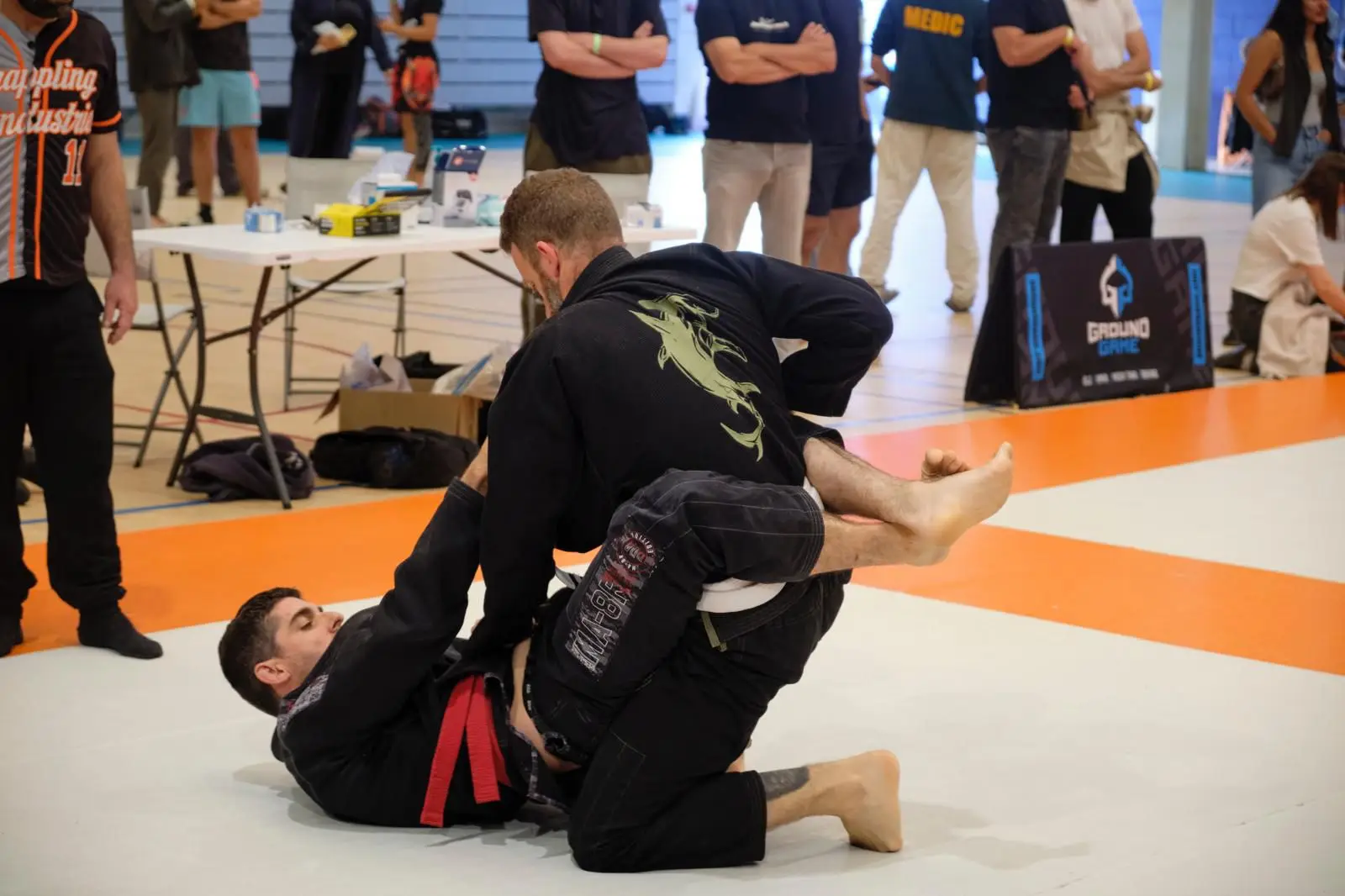 Compétition de jiu-jitsu brésilien : un pratiquant de BJJ Spirit au sol en garde, son adversaire en kimono noir tente le passage.