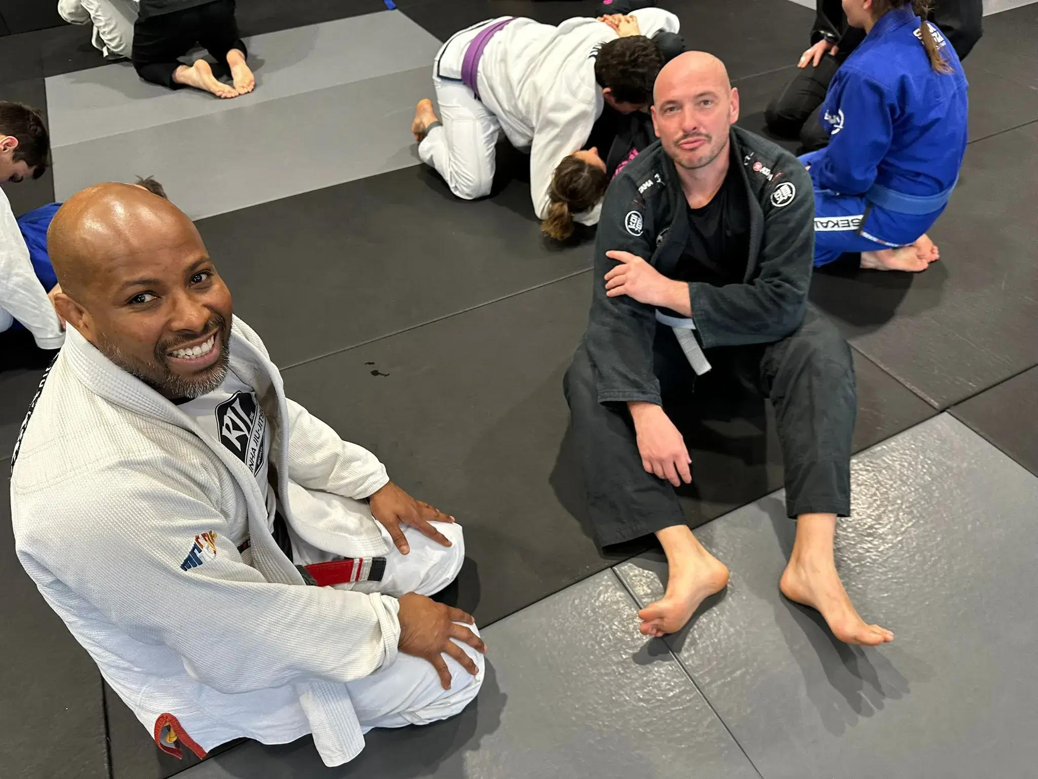 Deux pratiquants souriants assis sur le tapis.