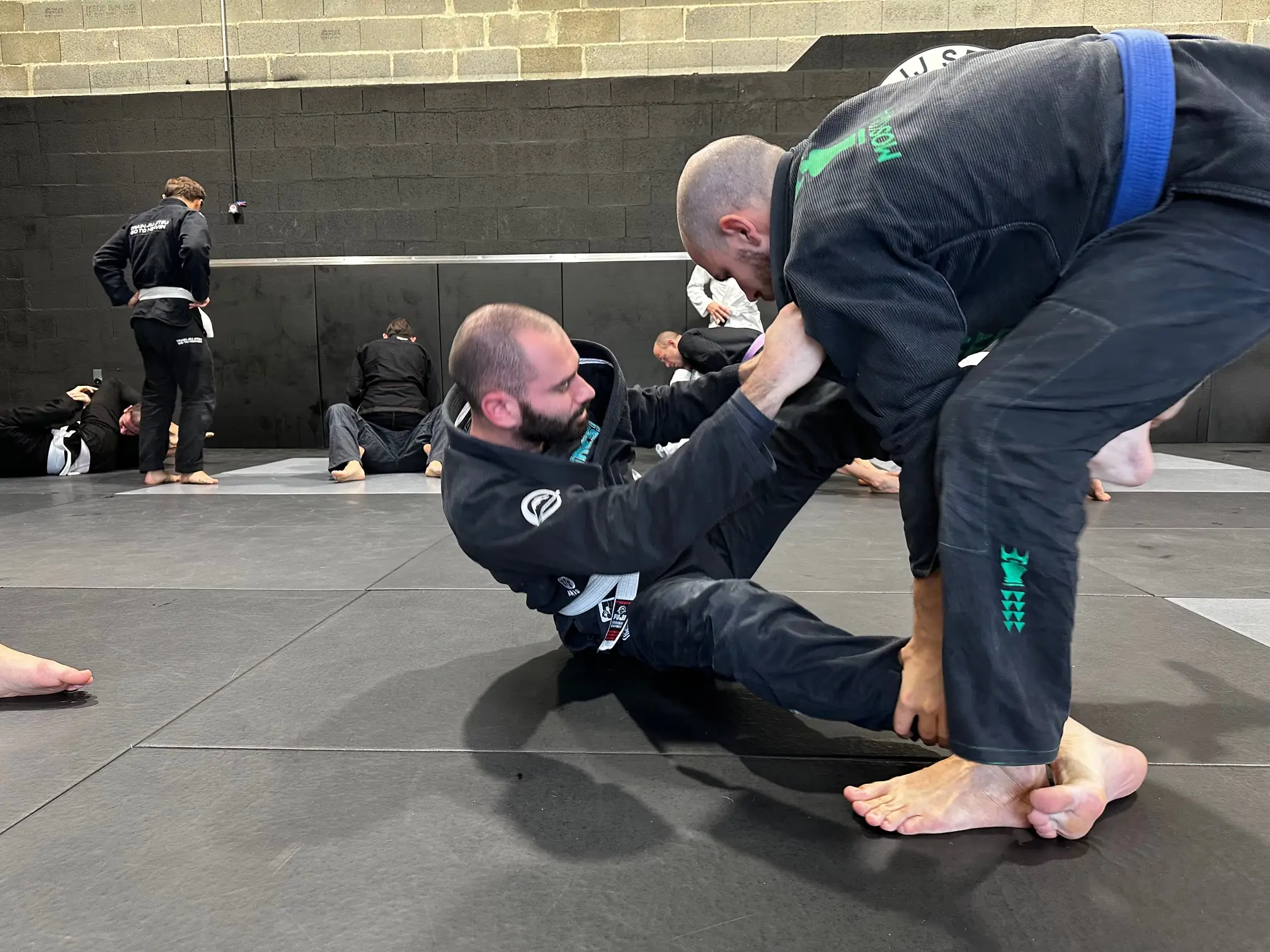 Cours de jiu-jitsu brésilien à BJJ Spirit : un pratiquant en garde assise saisit la cheville de son partenaire debout, sur le tapis du club.